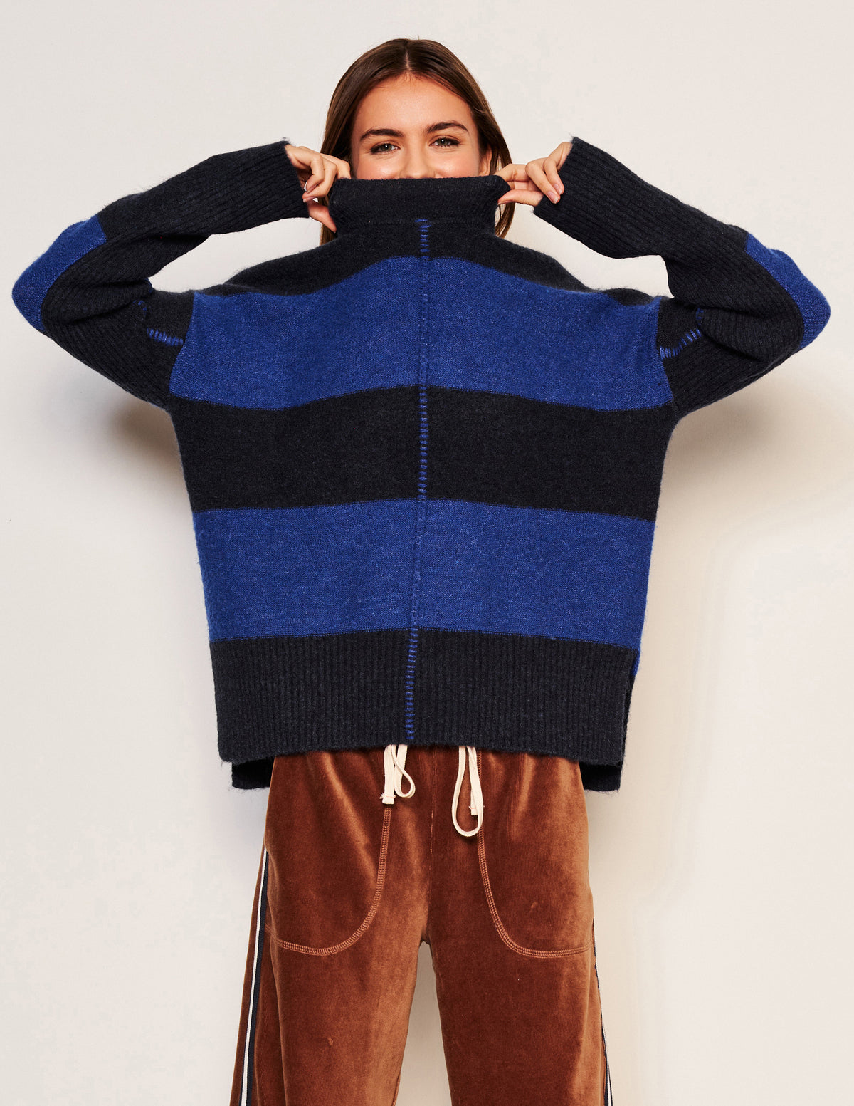 Sundry Bold Stripe Tunic Sweater in Deep Navy-model is pulling her sweater all the way up with her hands 