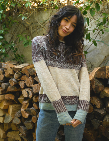Woman wearing a patterned sweater standing in front of stacked firewood.