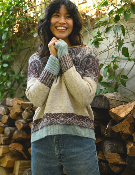 Woman wearing a patterned sweater standing in front of stacked firewood.
