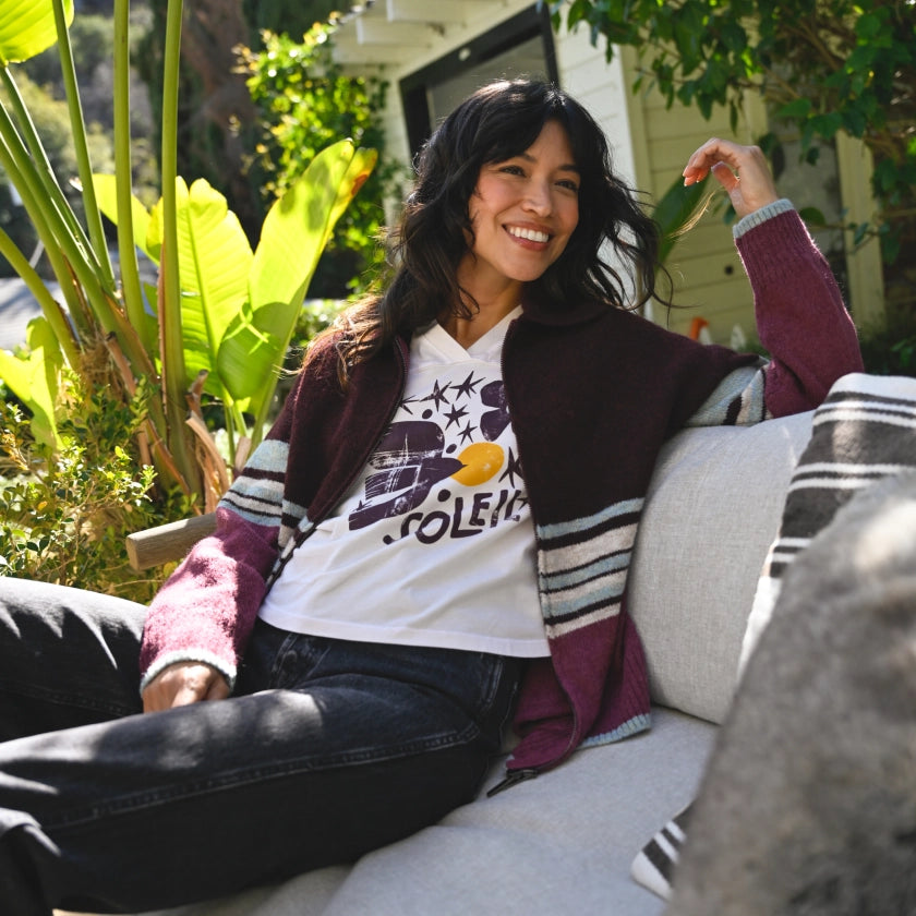 Woman sitting on a couch outdoors with plants and a house in the background