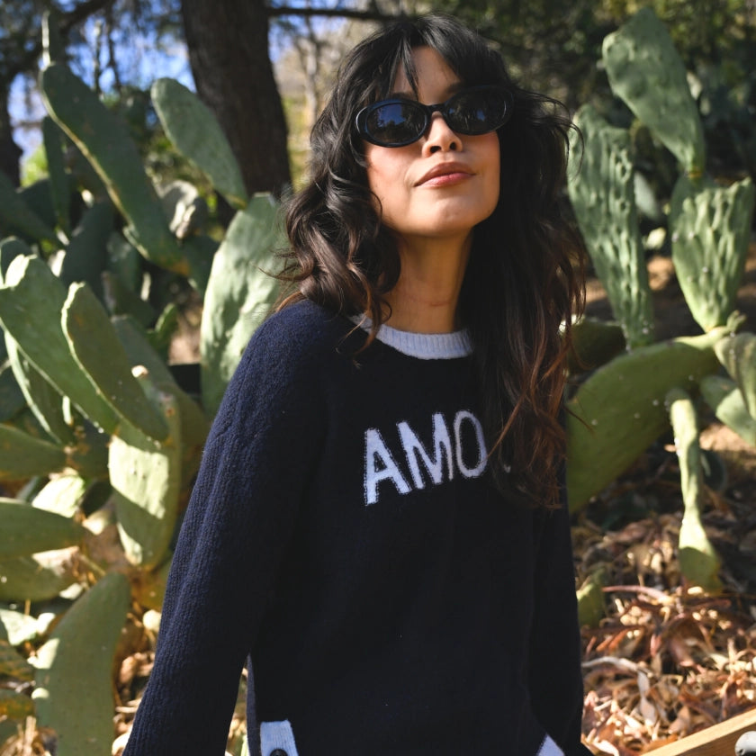 Woman wearing a sweater with 'AMOUR' text in front of cacti